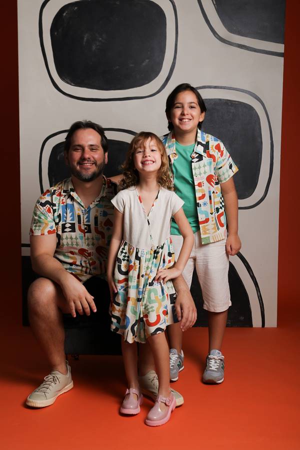 Pai com dois filhos. Eles usam roupas estampadas coloridas - Metrópoles