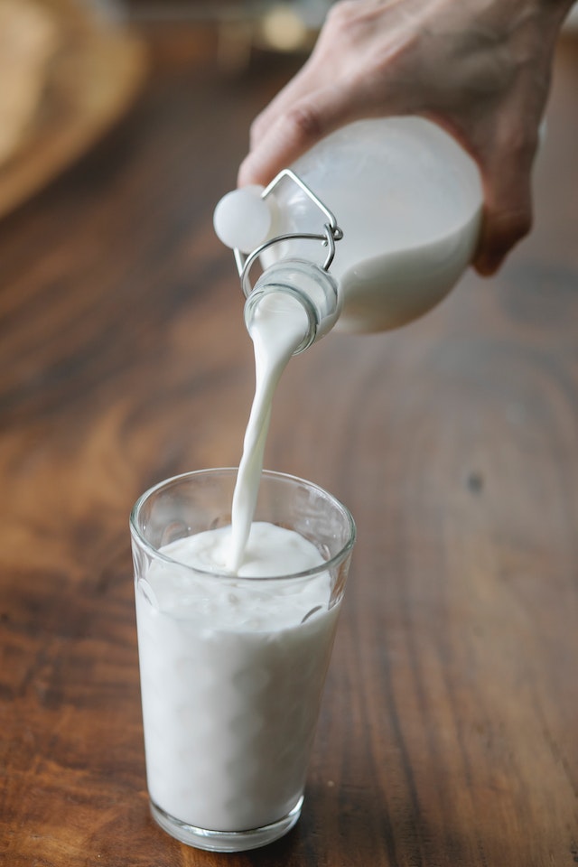 Mão despejando leite de garrafa de vidro em copo - Metrópoles