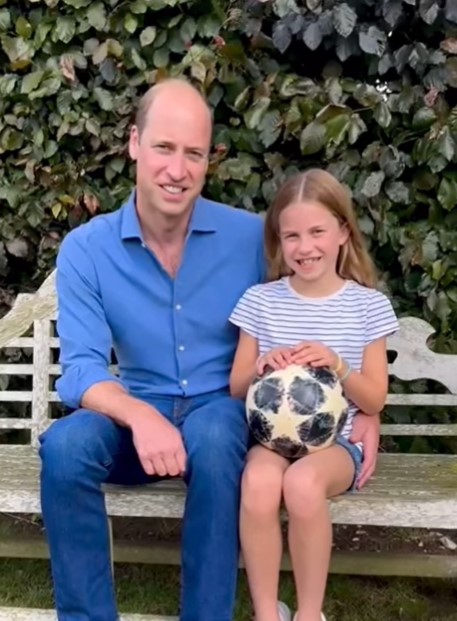 Frame de um vídeo em que o príncipe William aparece sentado ao lado da princesa Charlotte, que segura uma bola de futebol - Metrópoles