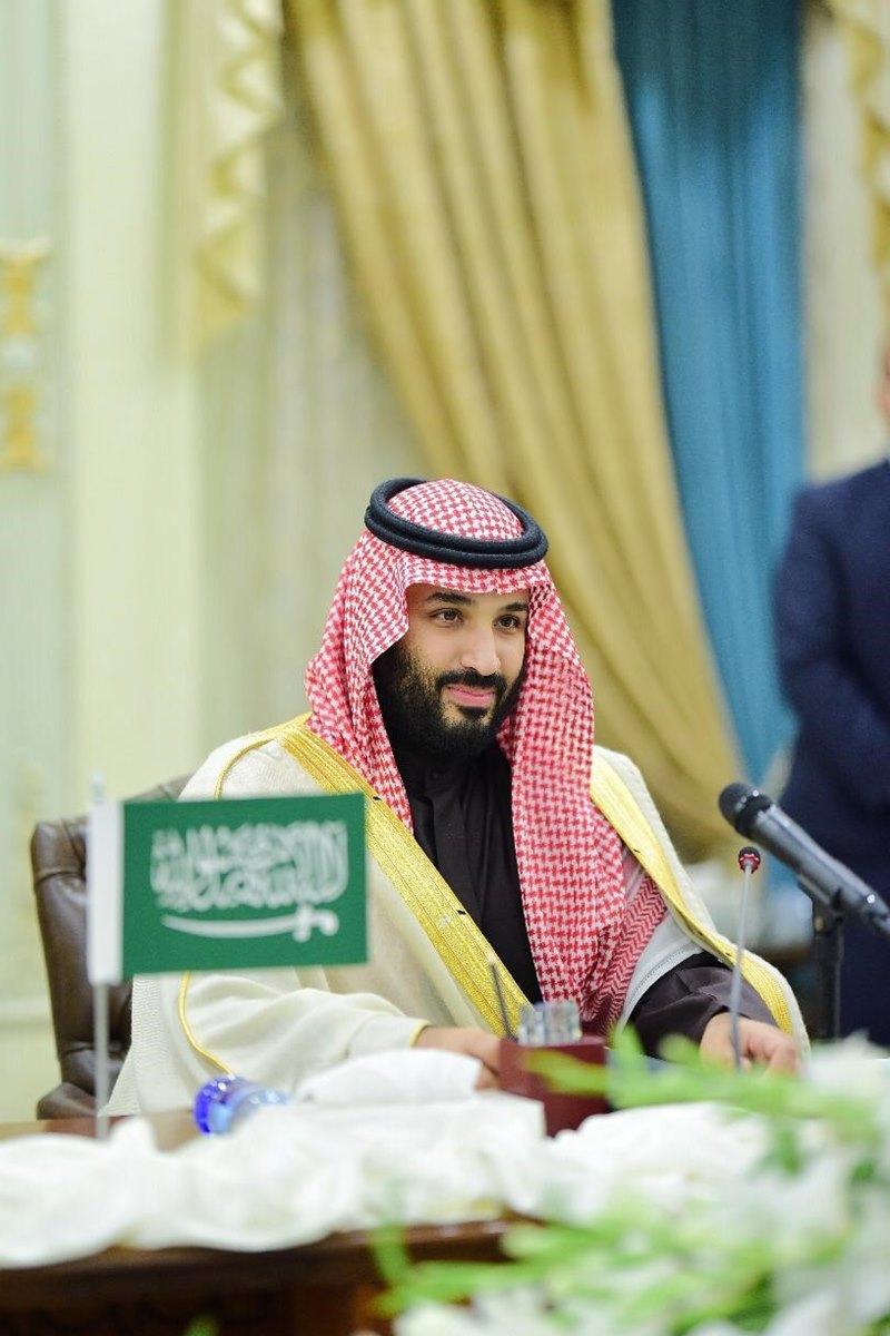 Foto colorida de homem pardo com veste mulçumanas masculinas e ao lado de uma bandeira da Arábia Saudita - Metrópoles