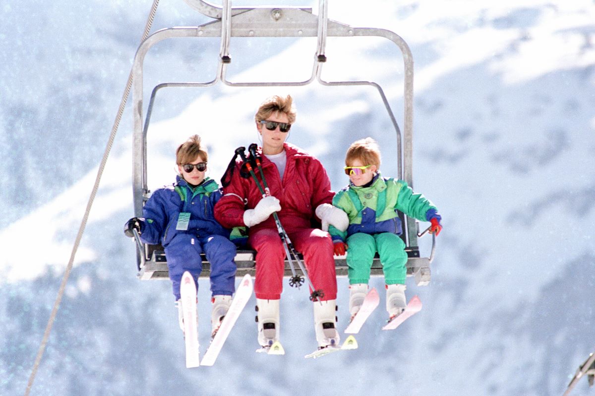 Foto colorida de dois meninos brancos e uma mulher branca em um carrinho de neve - Metrópoles