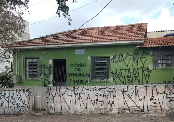 Imagem colorida de casa verde com muros pichados com tinta preta; "Chega de feminicídio", "justiça" e "paz" são frases vistas - Metrópoles