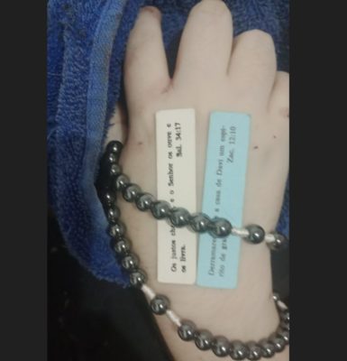 foto colorida de mão segurando terço e com bilhetes com trechos bíblicos