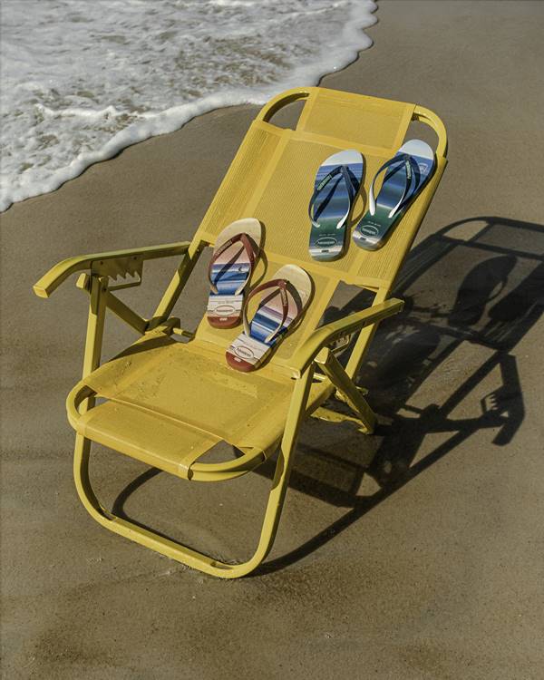 Chinelos em cadeira de praia amarela próxima ao mar, na areia da praia - Metrópoles