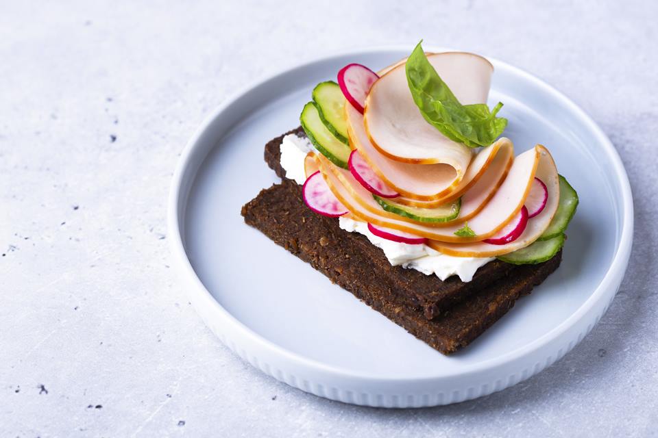 Foto colorida de um sanduíche aberto de pão de centeio com presunto e legumes frescos - Metrópoles