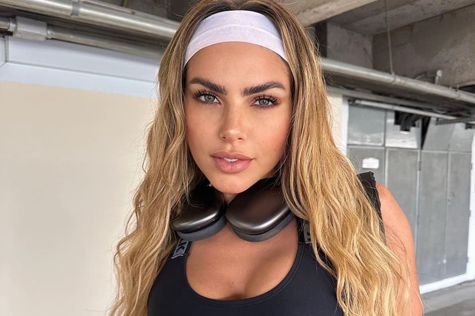 Erika Schneider posa com um top preto, uma faixa branca no cabelo e fones de ouvido - Metrópoles