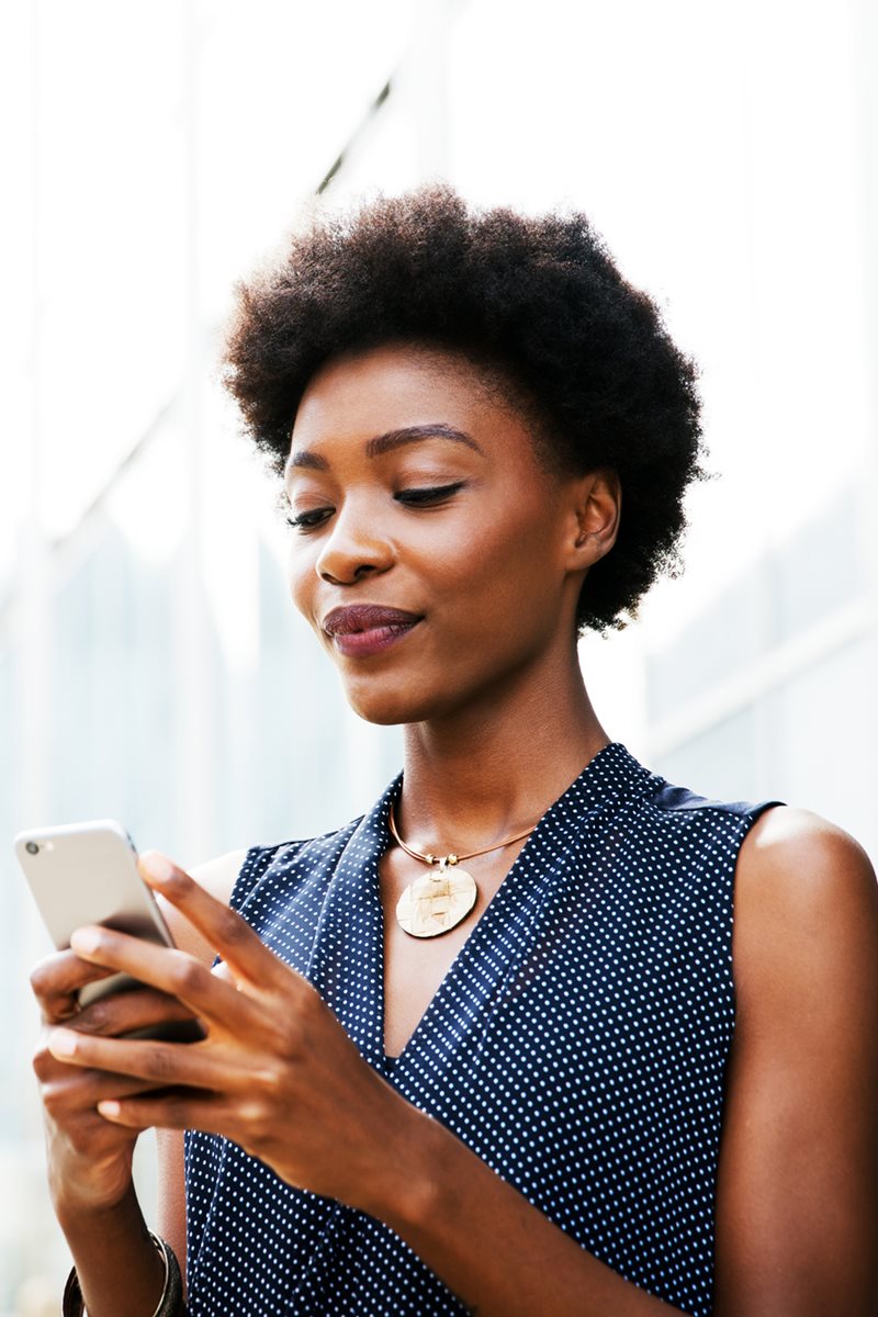 Foto colorida de mulher negra olhando o celular. Ela está 
