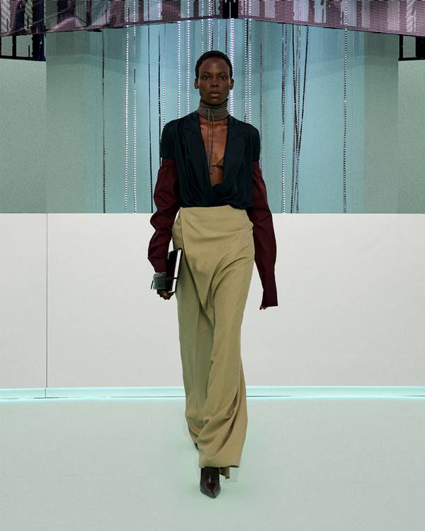 Em desfile de moda, modelo usa look com decote em azul e saia bege longa. As mangas são bordô - Metrópoles
