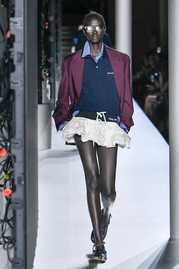 Na passarela de moda, modelo usa camisa azul gola polo, jaqueta roxa e minissaia branca - Metrópoles