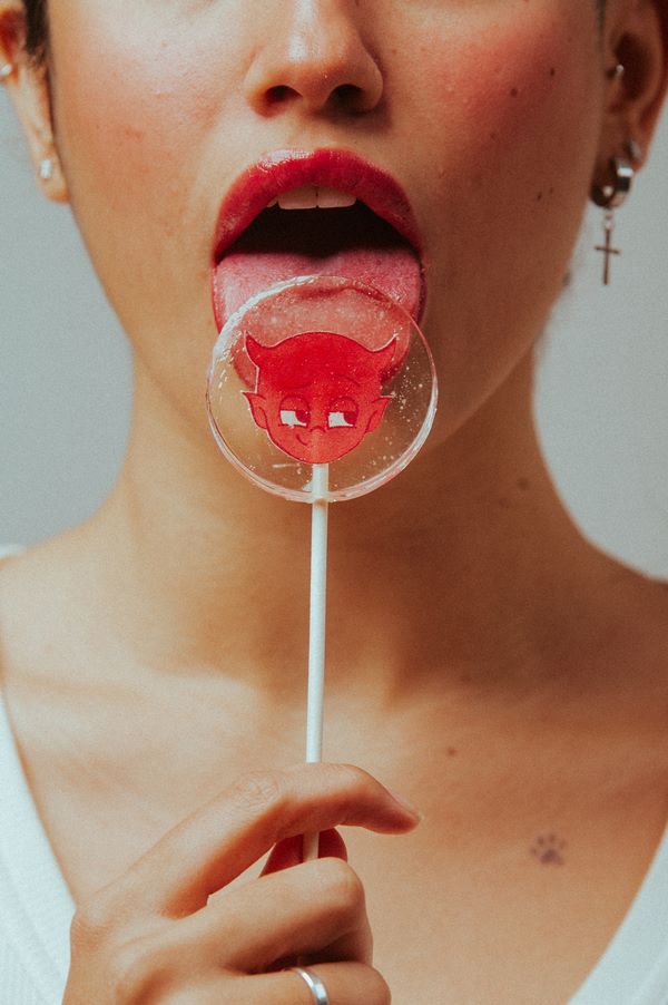 Na imagem com cor, mulher com a lingua para fora segura pirulito - Metrópoles