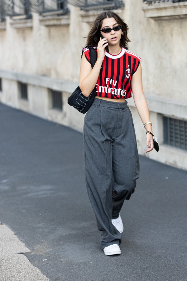 Mulher caminha pela rua usando camisa do Milan, bolsa preta e calça de alfaiataria cinza - Metrópoles