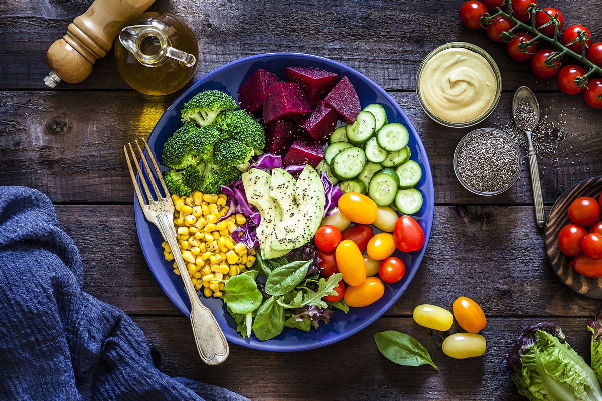 Imagem colorida mostra uma mesa vista de cima. Há um prato com vários alimentos saudáveis. Na parte externa, há alguns molhos, azeite e um garfo - Metrópoles