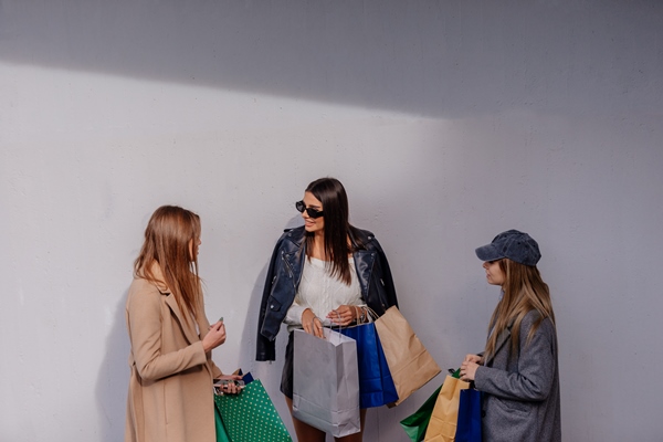 Três mulheres bem vestidas conversam e seguram sacolas de compras - Metróples