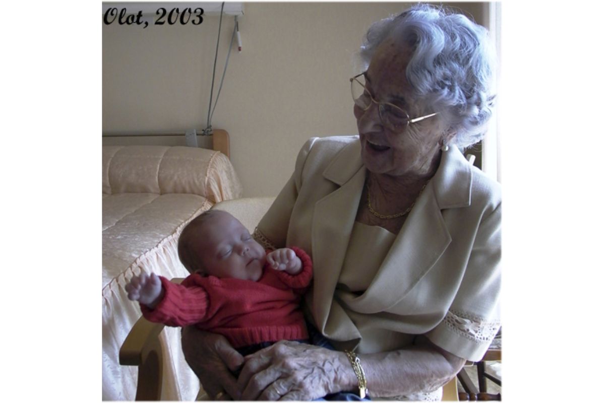 Foto colorida de bebê no colo de idosa, sentada e sorridente - Metrópoles