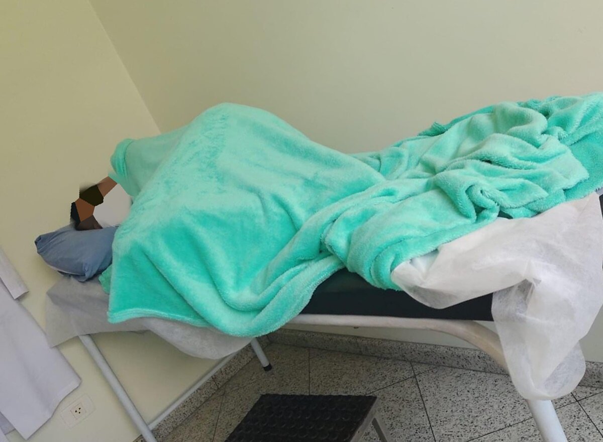 Em foto colorida mulher em maca de hospital coberta com lençol azul marinho - Metrópoles