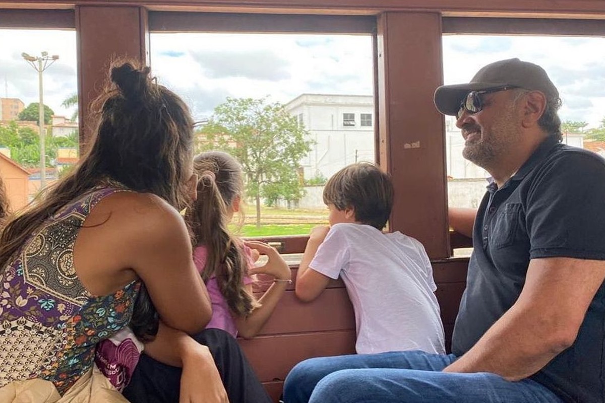 Foto colorida de mulher e homem com duas crianças sentados. Eles olham pela janela de um trem - Metrópoles