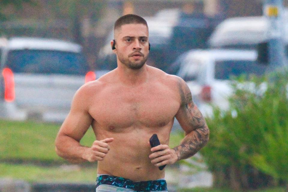 Foto colorida de Rodrigo Godoy correndo na praia sem camisa - Metrópoles