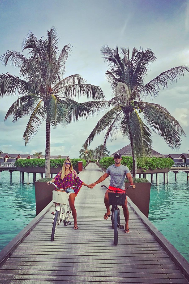 Foto colorida de homem e mulher, parados, em cima de uma bicicleta. Ele estão de mãos dadas - Metrópoles