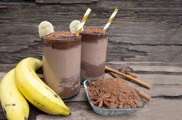 Vitamina de iogurte de chocolate misturados com banana, leite, bebidas com alto teor de proteína, whey, colocados um copo em um fundo de madeira.