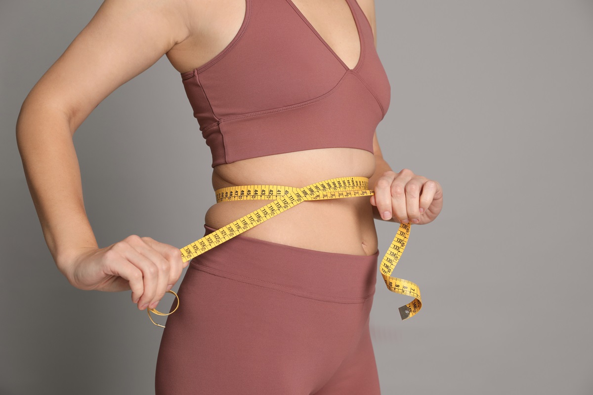 Foto colorida de mulher com fita métrica na barriga. Ela usa um cropped e uma legging - Metrópoles