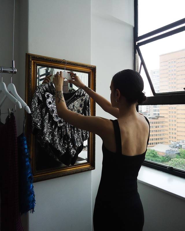 Mulher segura peça de roupa em cabide em frente a um espelho - Metrópoles