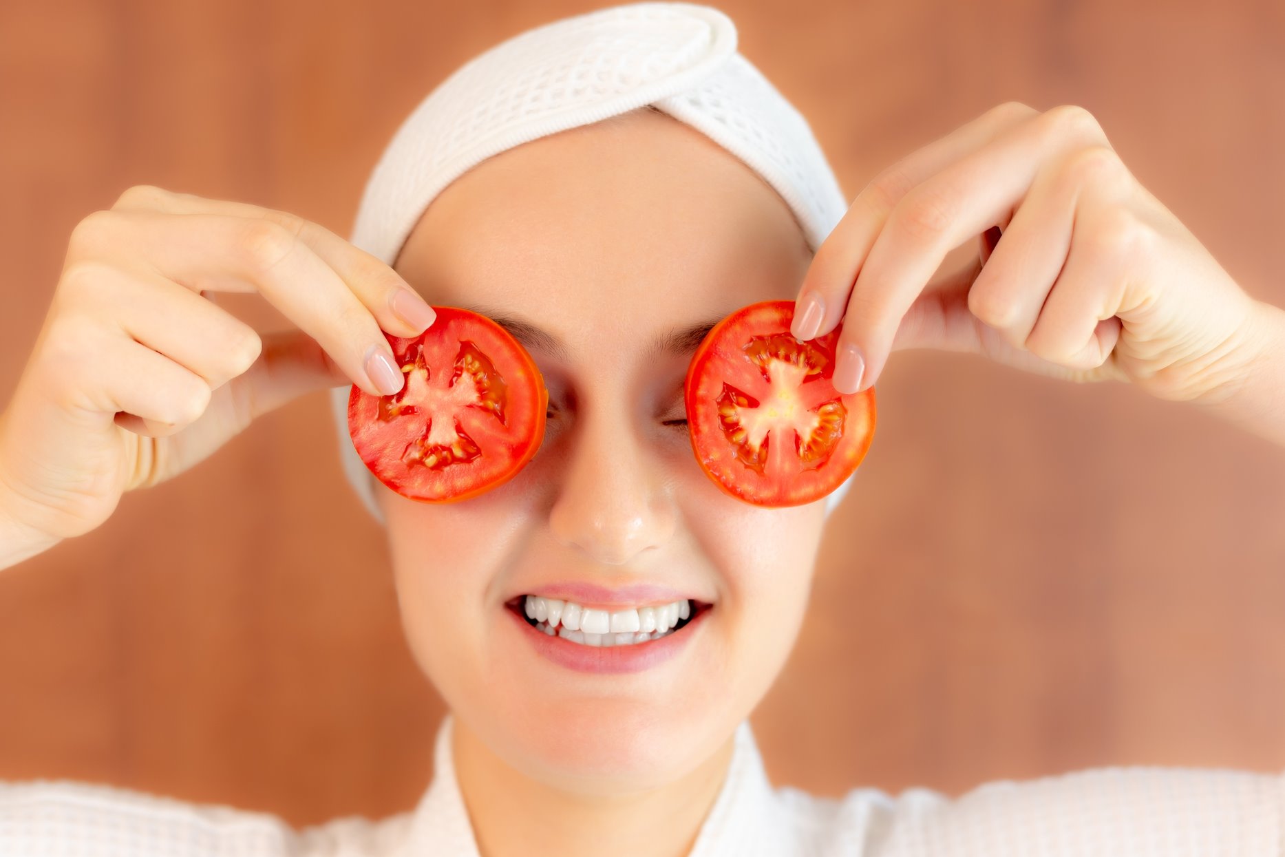 Foto colorida de mulher segurando duas fatias de tomate na altura dos olhos - Metrópoles