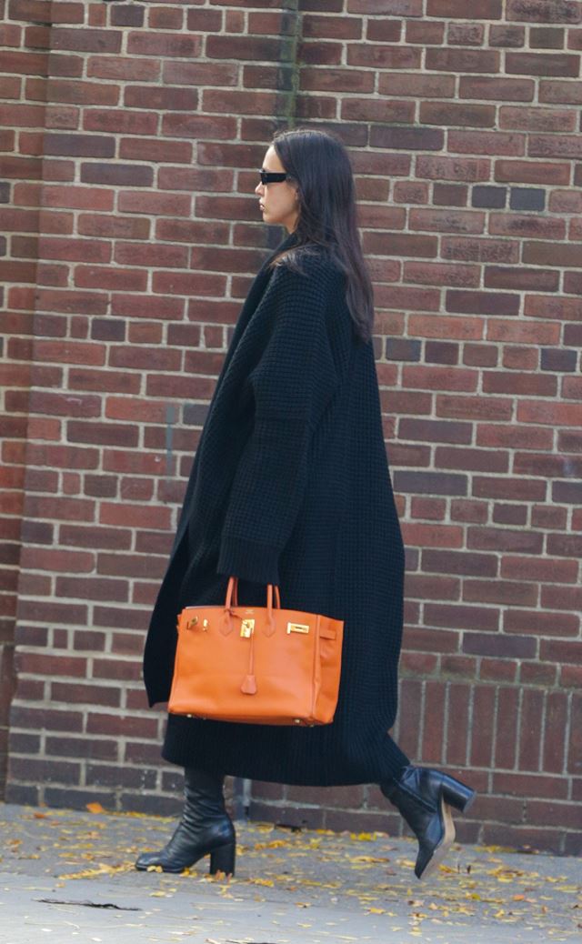 Na imagem com cor, mulher anda na rua com look preto e bolsa laranja - Metrópoles