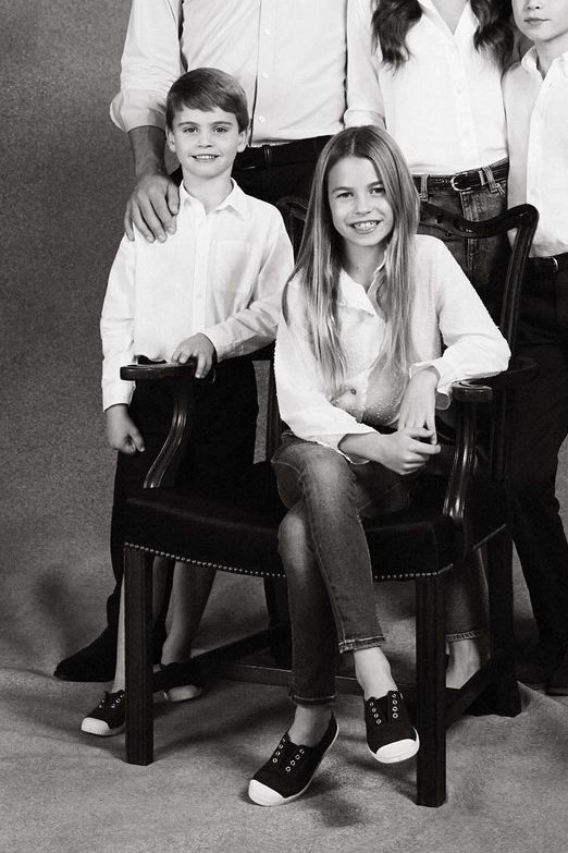 Foto em preto e branco de menino em pé e de menina sentada em uma cadeira - Metrópoles