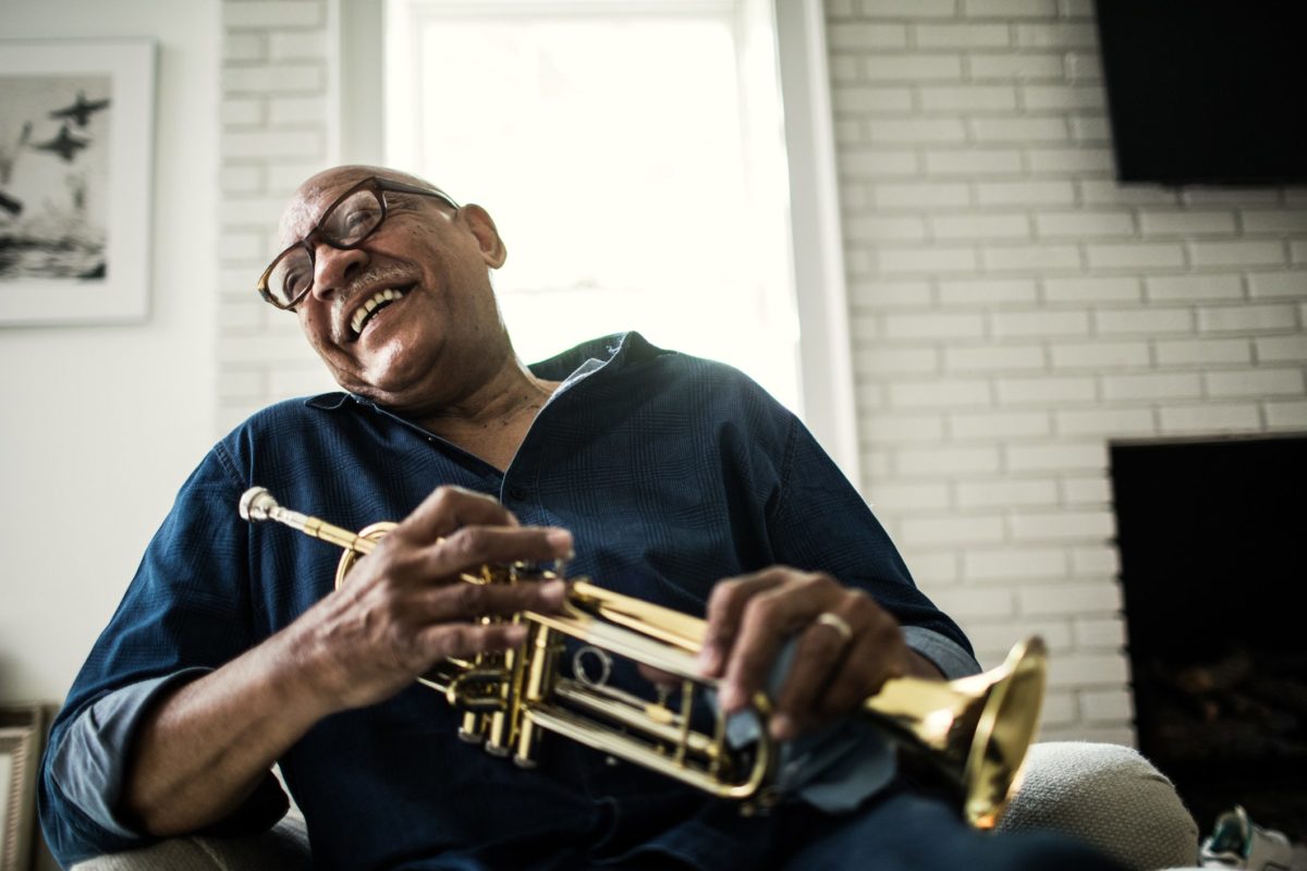 Foto mostra homem idoso sorrindo com um trompete nas mãos