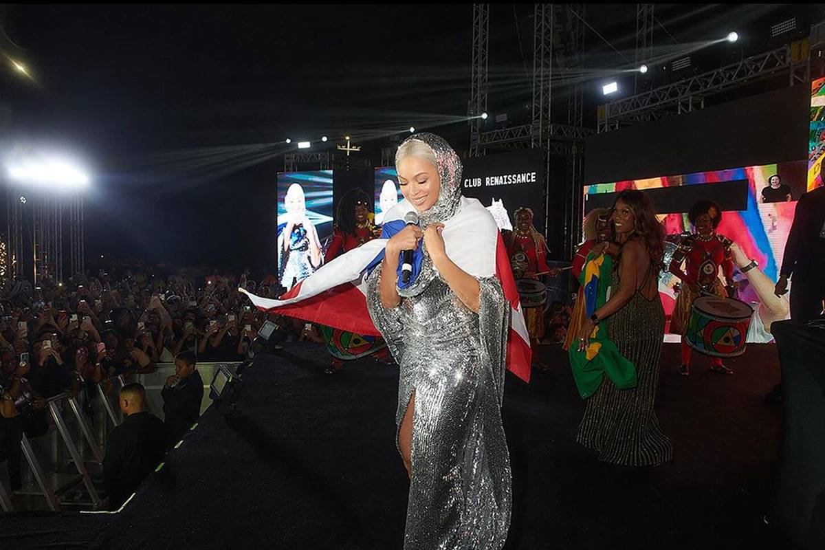 Foto de mulher em palco cantando. Ela está coberta com uma bandeira - Metrópoles