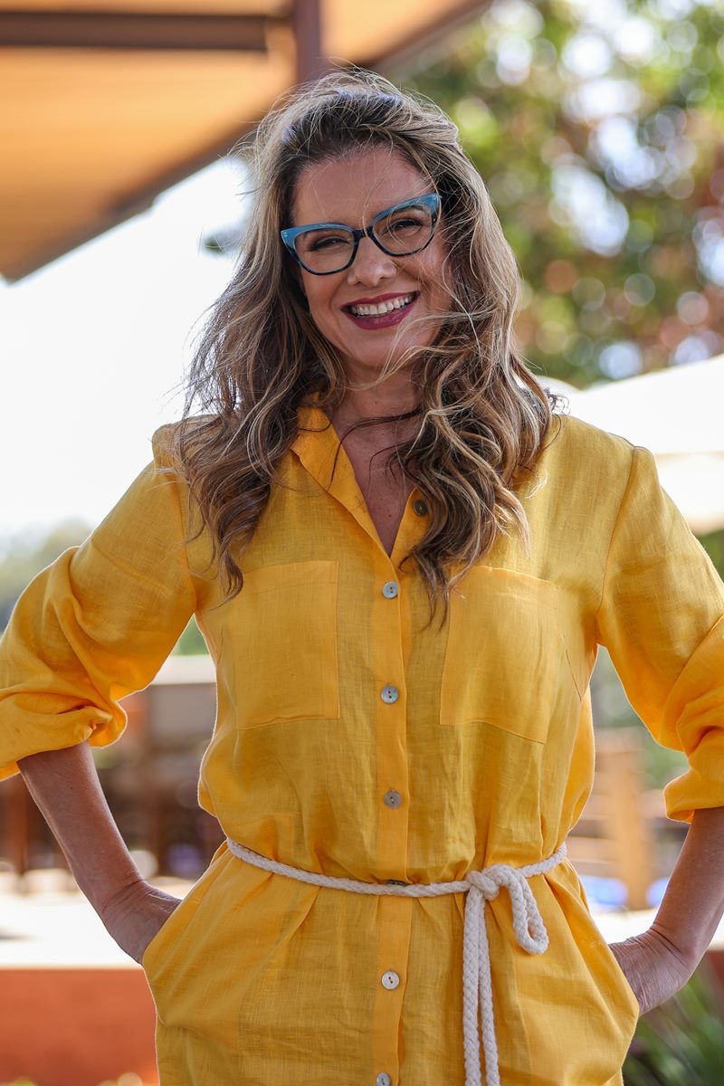 Foto de mulher de óculos, sorridente e com as mãos no quadril. Ela usa uma blusa amarela - Metrópoles