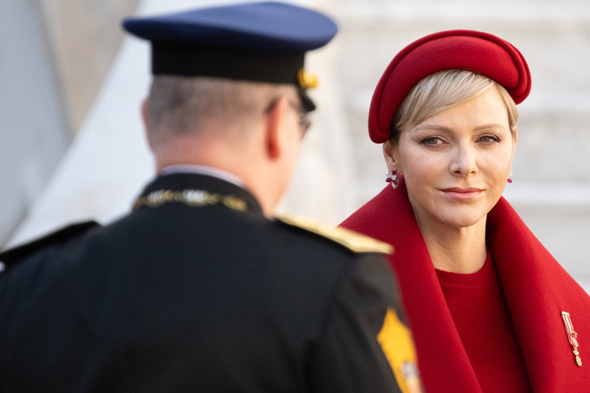 Foto de mulher com roupa vermelha olhando para homem, com trajes militares. Ele está de costas - Metrópoles