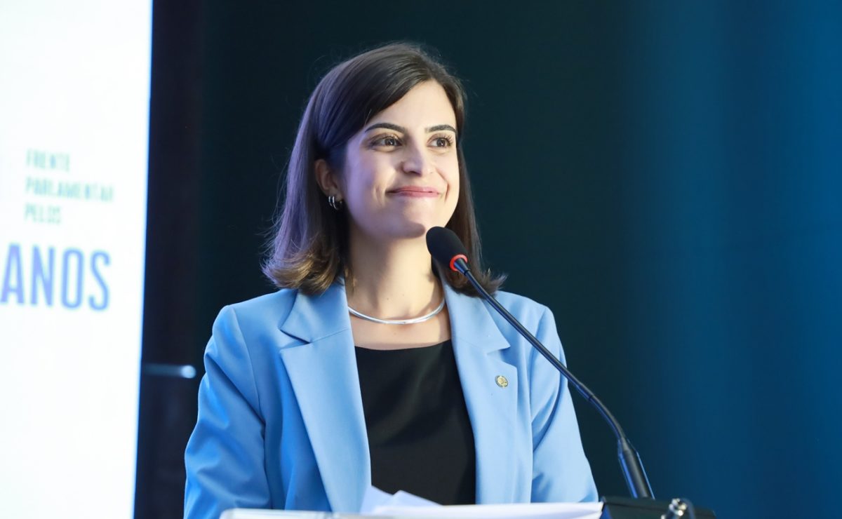 Imagem colorida mostra Tabata Amaral, mulher branca, de cabelos pretos, de terno azul e blusa preta, em imagem do peito para cima, na frente de um microfone - Metrópoles