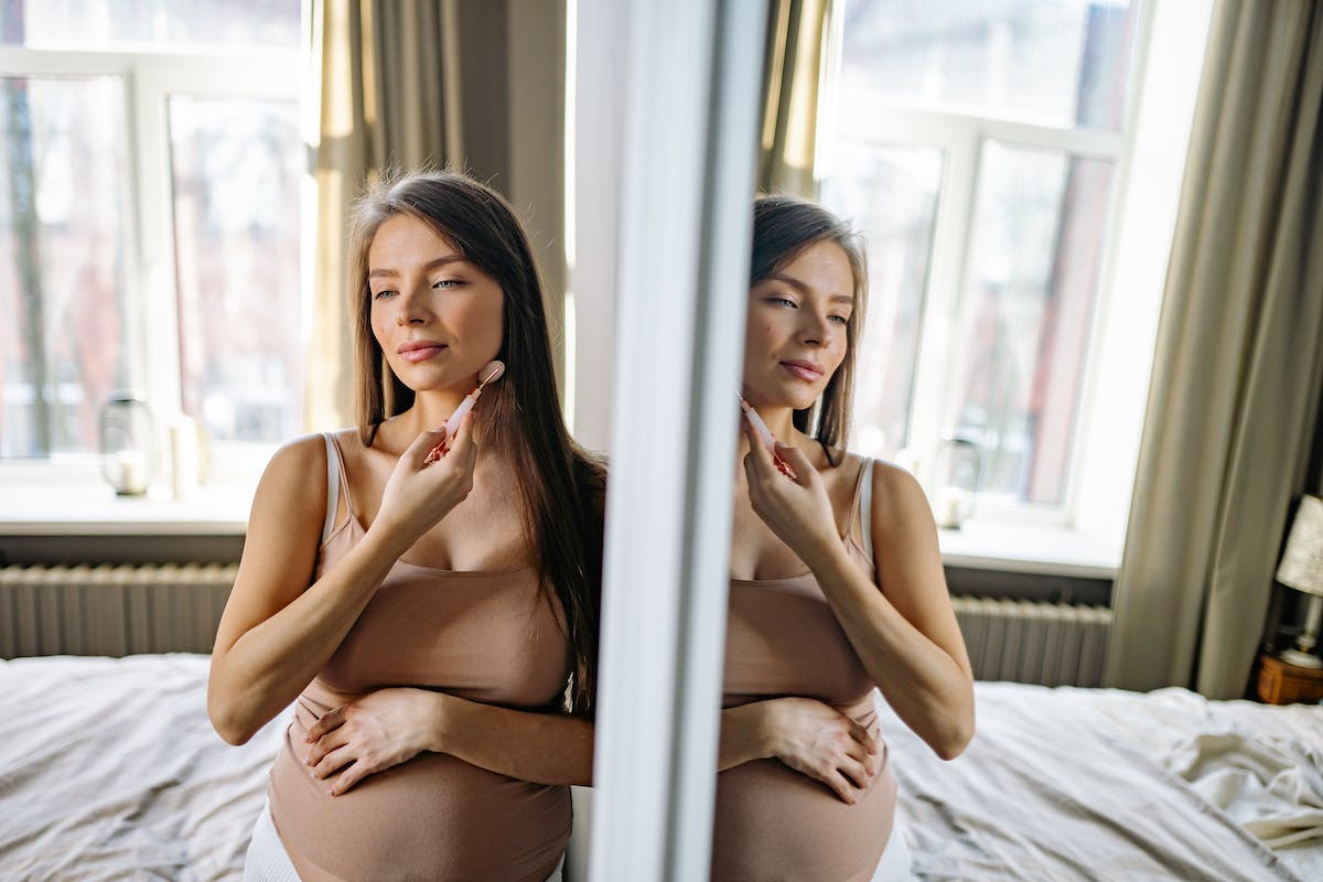 Jovem grávida cuidando da pele do rosto em quarto
