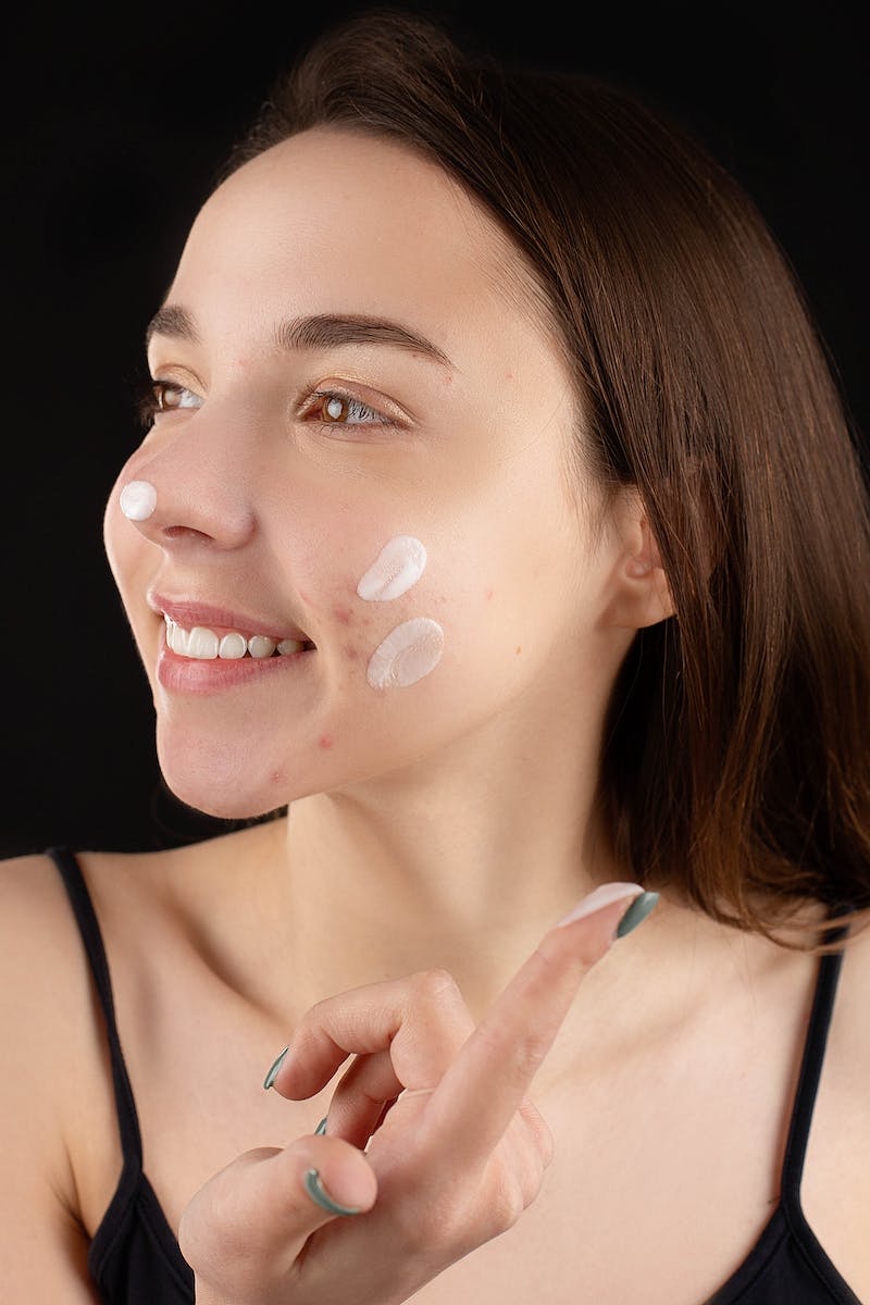 Jovem mulher branca olhando para o lado aplicando creme hidratante no rosto - Metrópoles