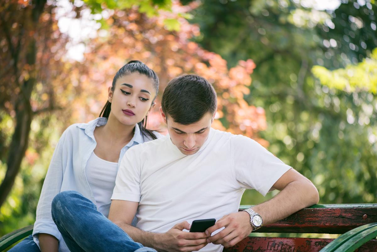 Foto colorida de um casal sentado olhando no celular - Metrópoles
