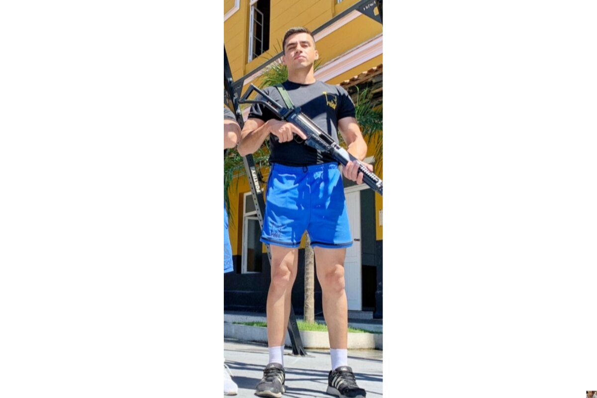 Soldado com roupa de treino da PM posa com fuzil, apontado para baixo, dentro de batalhão - Metrópoles