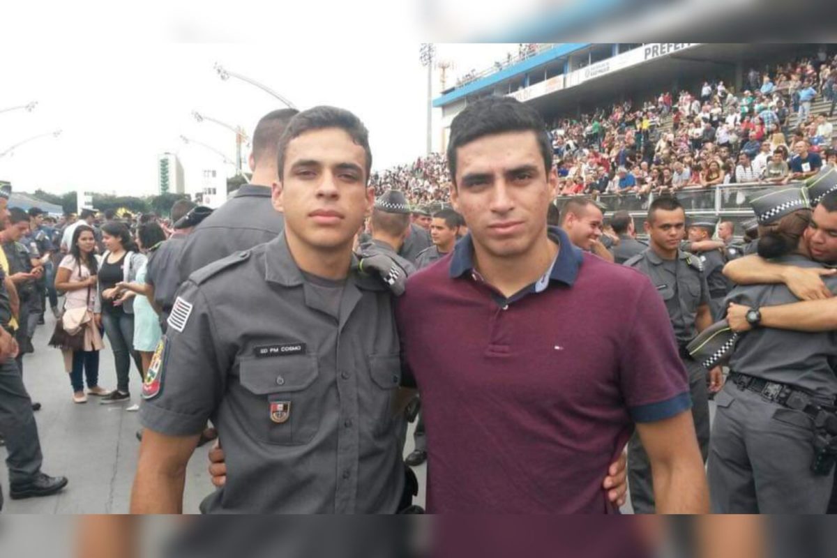 Imagem colorida de dois jovens abraçados próximos a uma multidão - Metrópoles