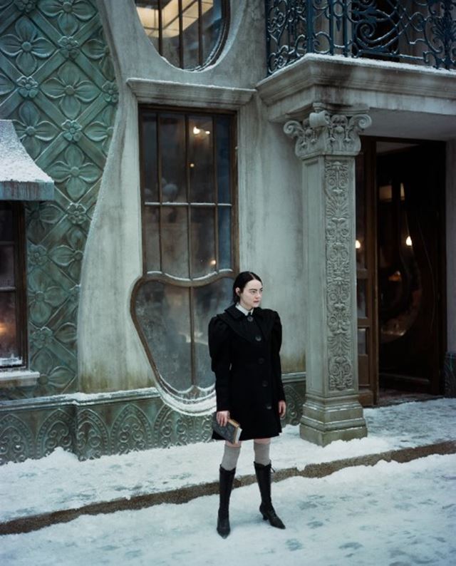 Emma Stone em Pobres Criaturas. Ela usa um vestido preto com mangas estruturadas e bota longa - Metrópoles