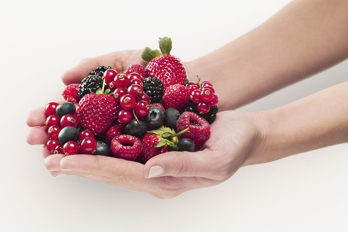 Mão feminina segurando um punhado de frutas vermelhas