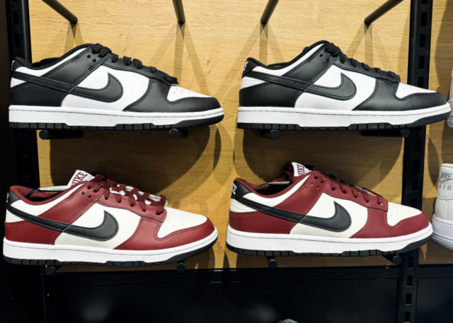 Nike Dunks Low em prateleira de loja. Dois modelos em preto e branco, os outros estão nas cores vermelha, branco e o preto apenas no swoosh e calcanhar.