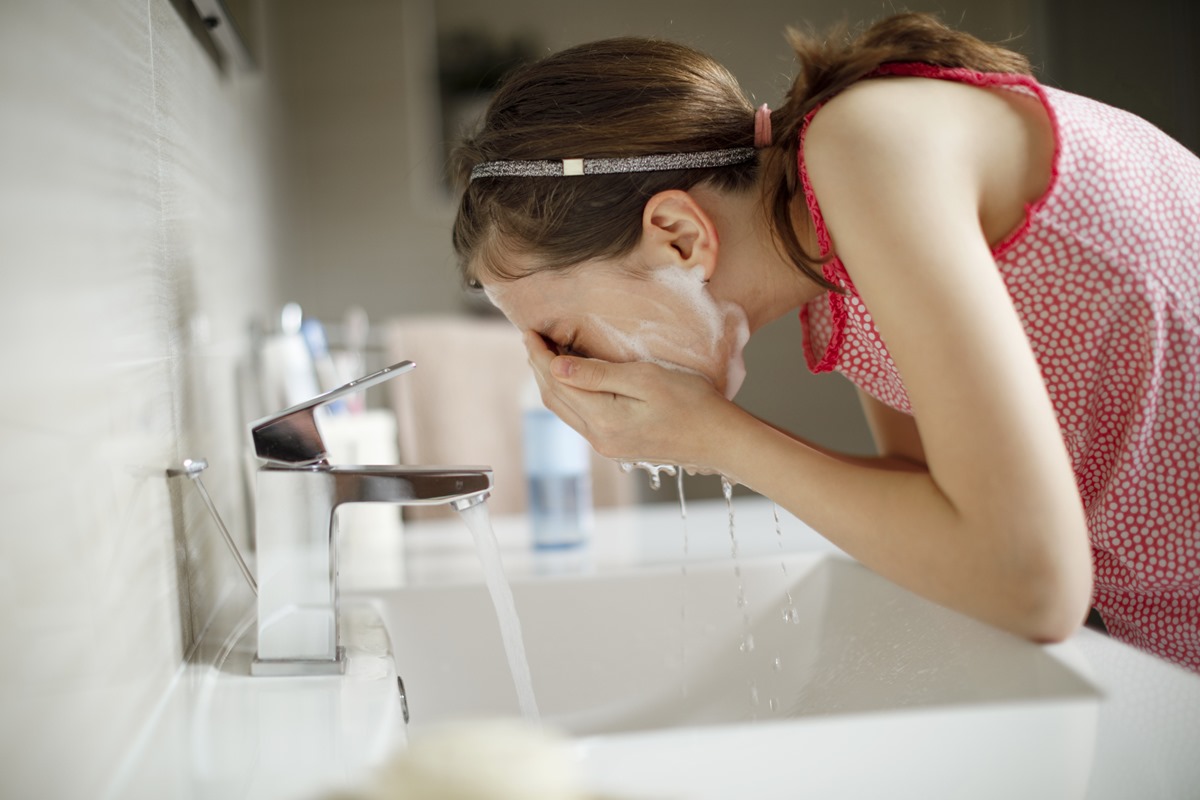 Jovem adolescente lavando o rosto em pia de banheiro - Metrópoles