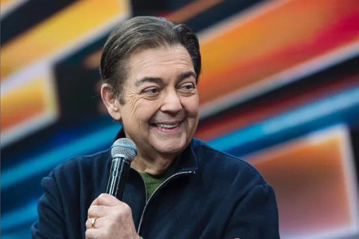 Foto colorida de Faustão. Ele segura um microfone e está sorrindo - Metrópoles