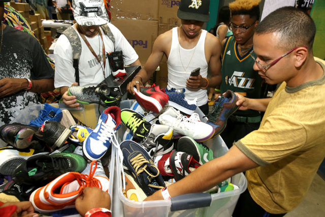 Homens observam calçados de variadas cores e modelos postos dentro de caixas de plástico.