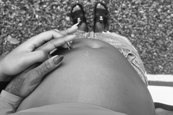 Imagem em preto e branco de barriga de mulher grávida e mãos do casal lésbico - Metrópoles