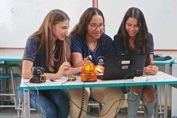 Três garotas adolescentes usam um computador em uma sala de aula