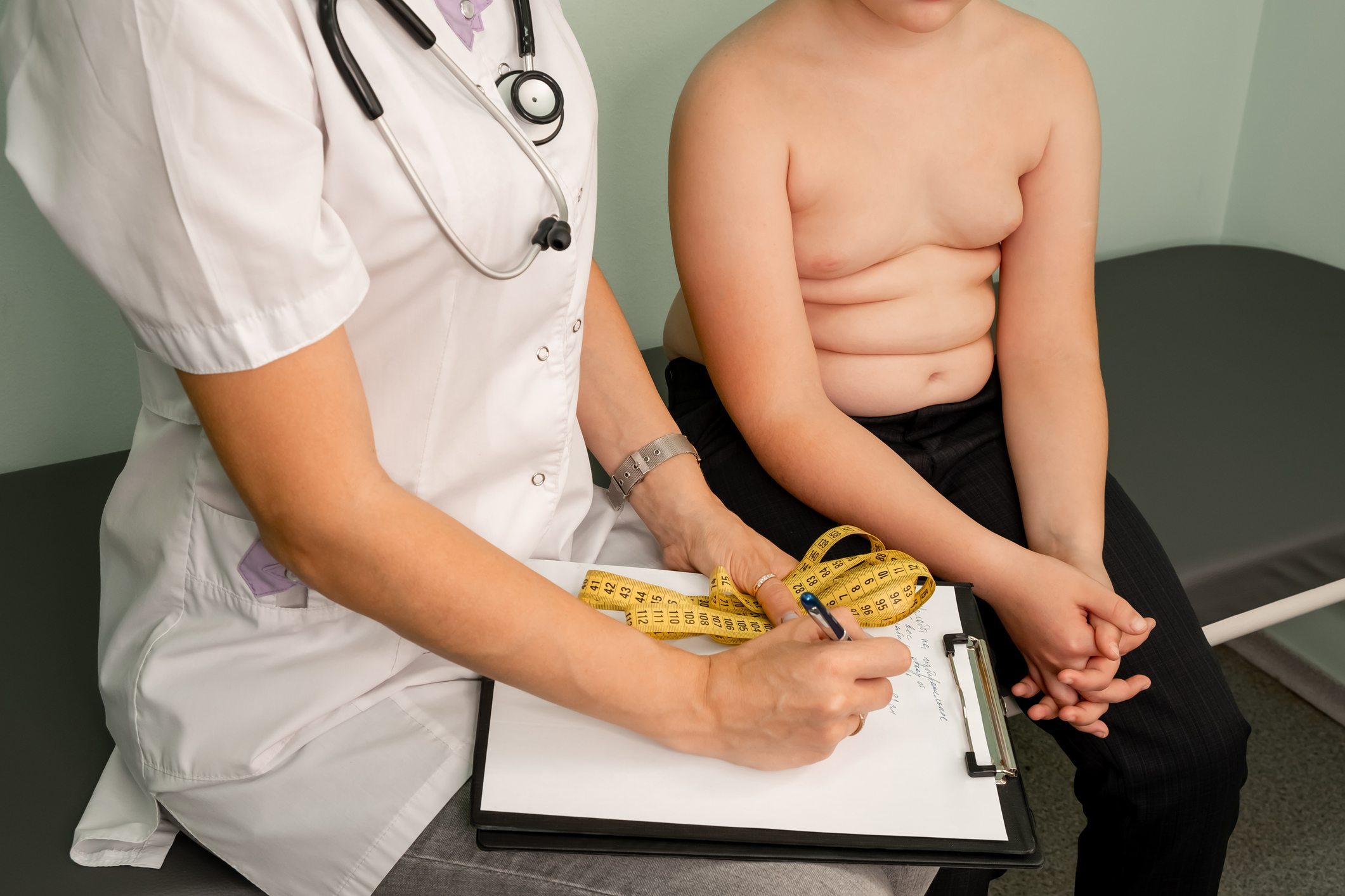 Foto mostra criança com obesidade sobre maca enquanto médica a examina