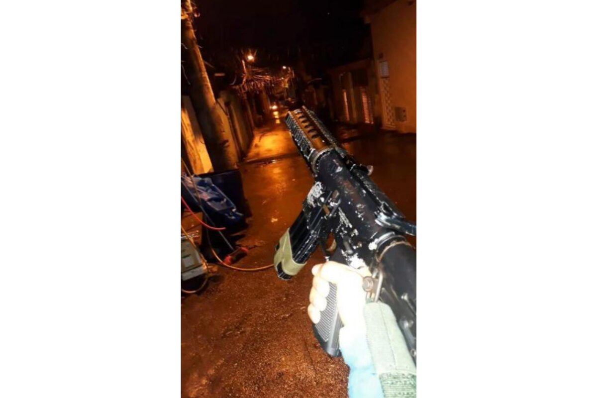 Imagem colorida de mão segurando fuzil no meio de uma rua - Metrópoles
