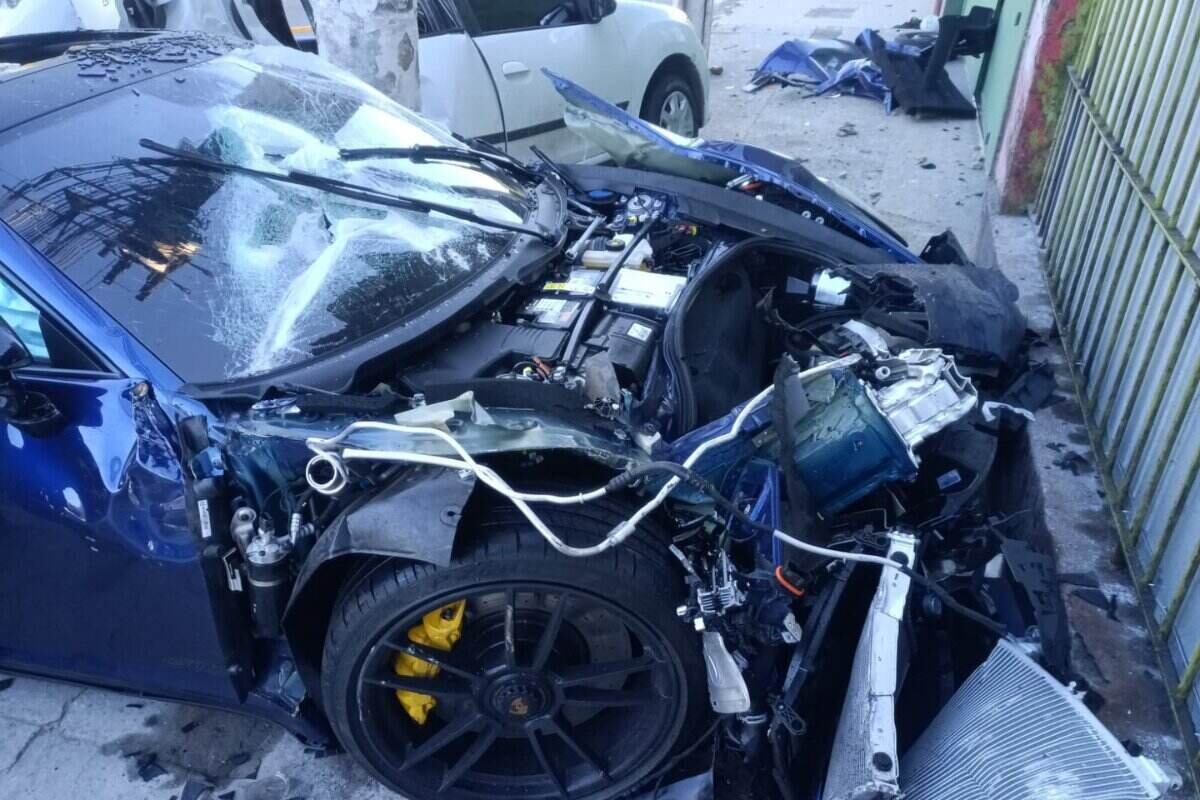 Foto colorida de Porsche azul escuro com a dianteira destruída - Metrópoles