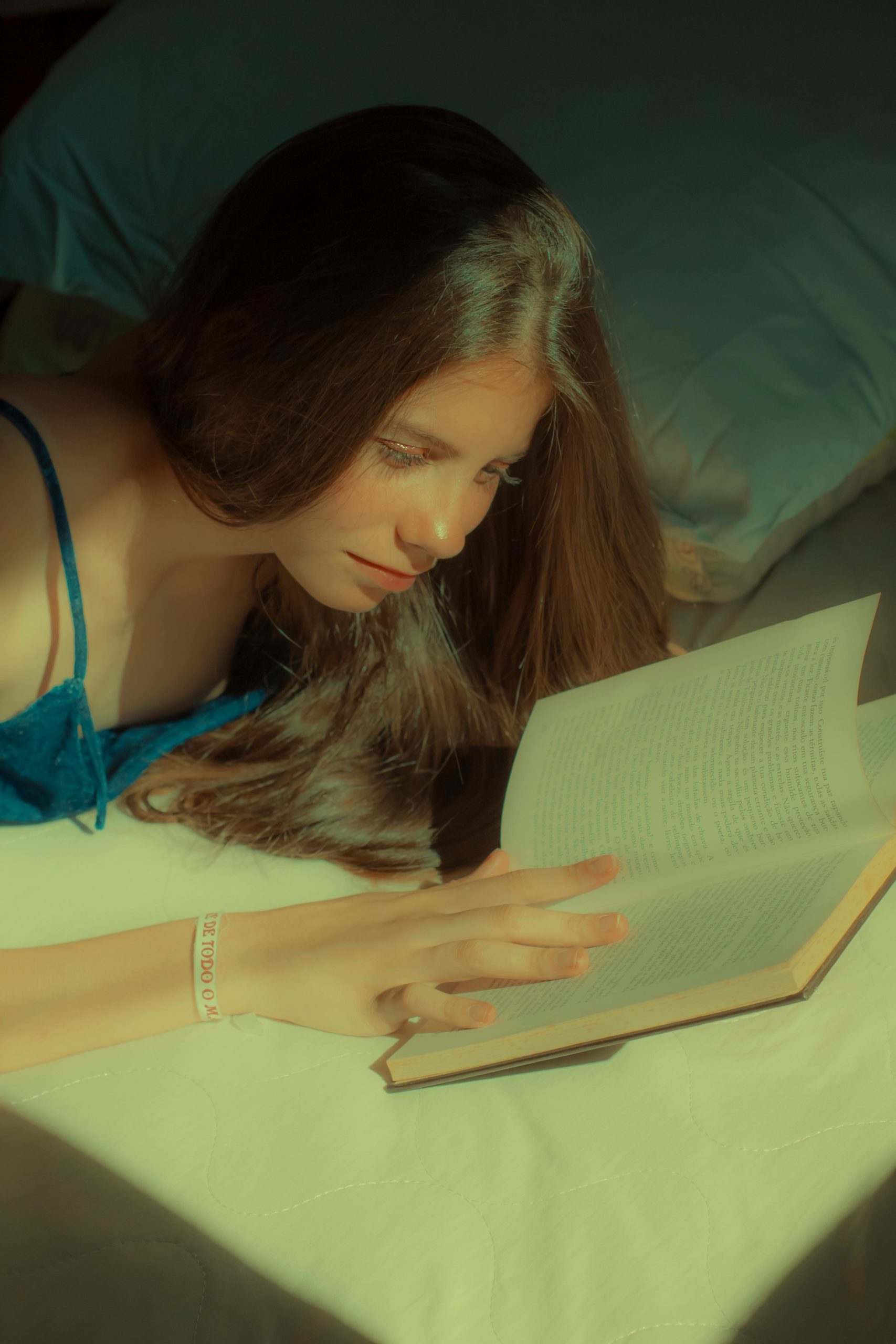 Jovem mulher deitada em cama lendo livro - Metrópoles